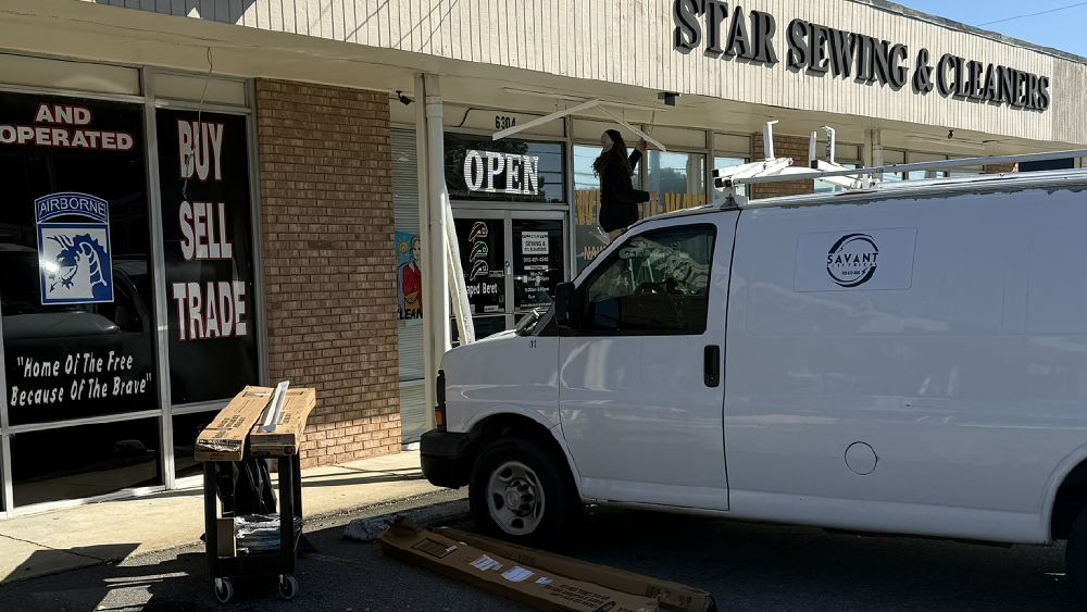 Branded Savant Electrical service van parked at a commercial storefront job with a crew member working on the storefront