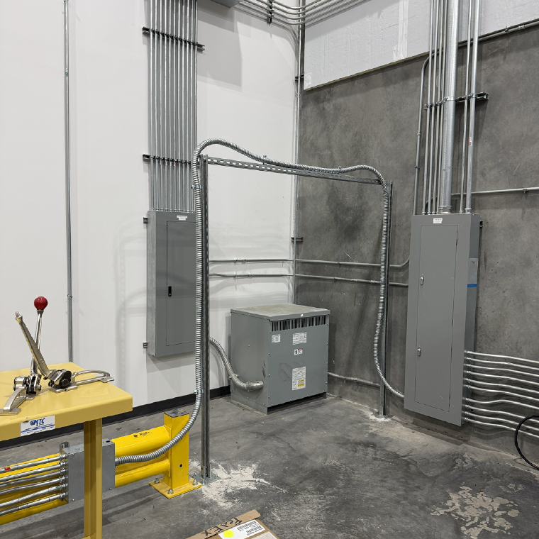 Parallel conduit racks feeding panelboards and a dry-type transformer in an industrial electrical room