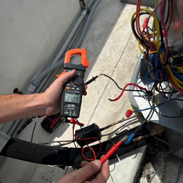 Electrician taking a clamp-meter reading at the wiring of a condensing unit