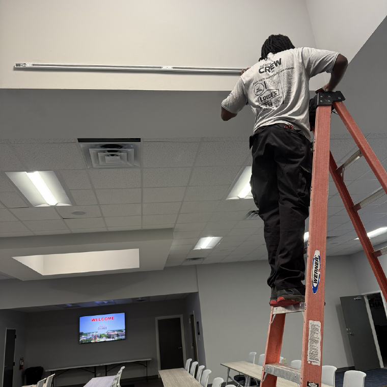 Savant electrician on a ladder installing track lighting at the Greater Fayetteville Chamber's new office
