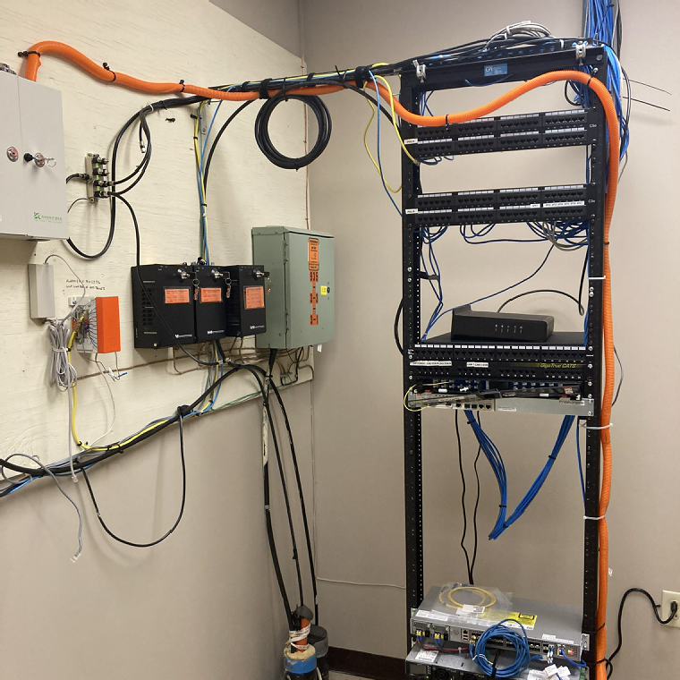 Telecom room backboard with patch panel rack, orange innerduct and fiber enclosure
