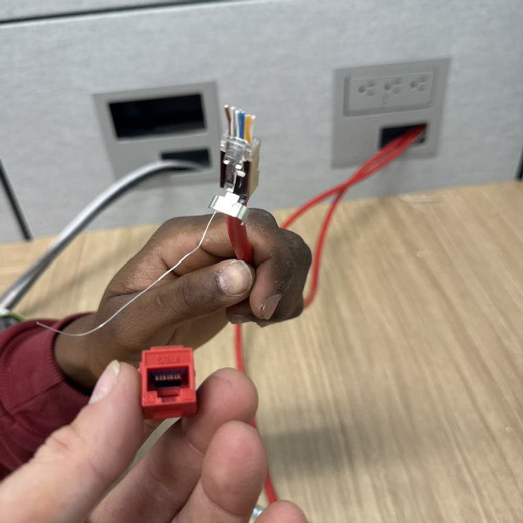 Hands terminating a category cable into a keystone jack at a device plate